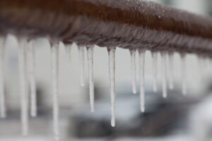 Icicles hanging from a brown pipe. Frozen water and metal surface, winter time concept. selective focus shallow depth of field
