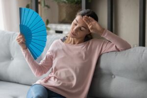 woman-sweating-on-couch-with-paper-fan-because-AC-is-out